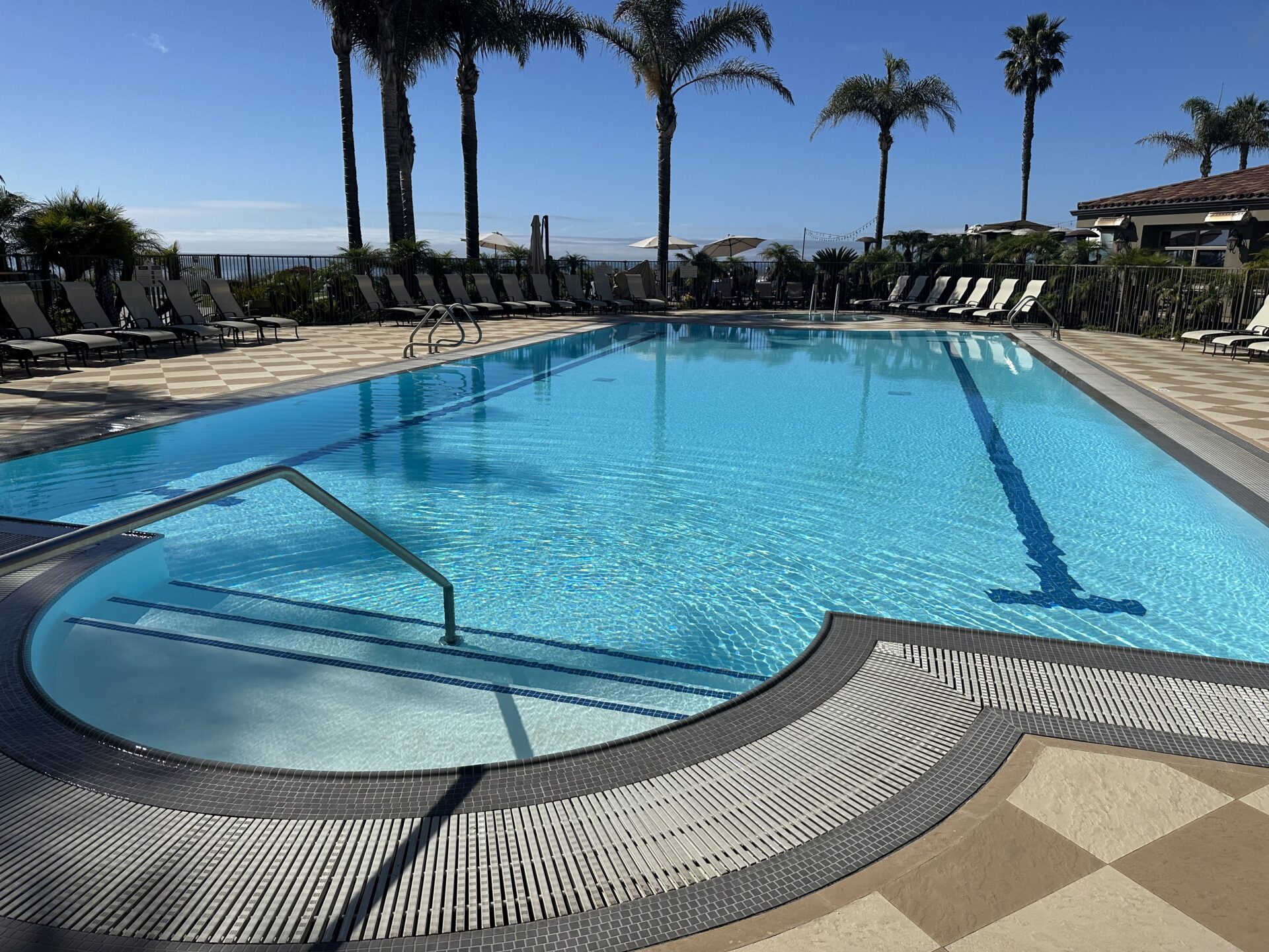 Resort lap pool with lane lines and loungers, with the ocean behind
