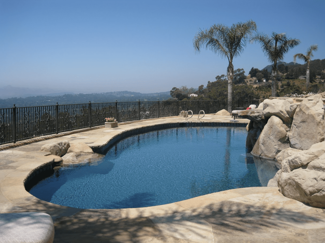 Freeform hillside backyard pool with a rock waterfall and an ocean view